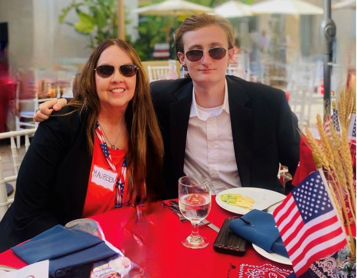 Woman and young man wearing sunglasses seated at a red table with American flag.