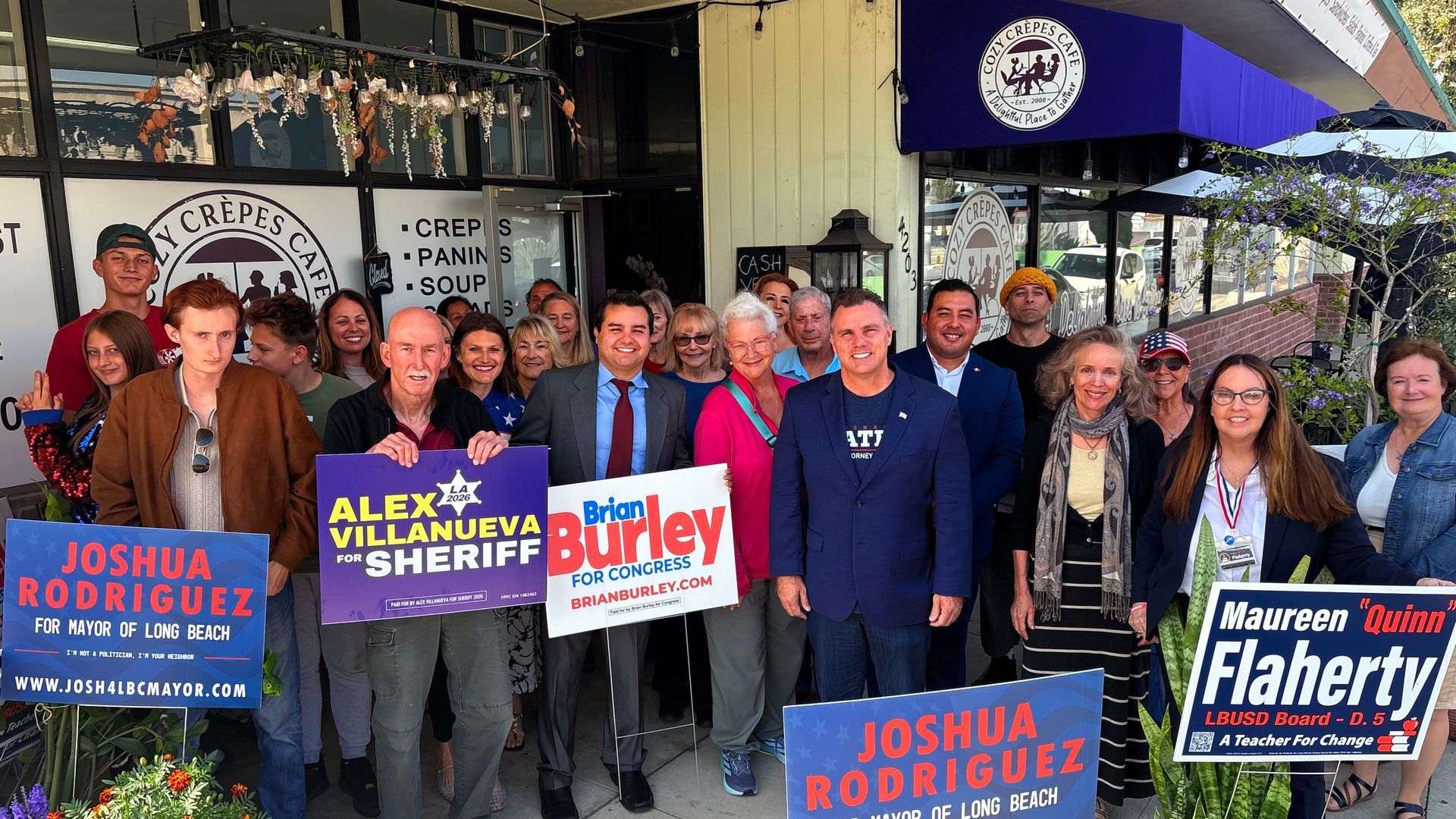 Group of people posing outside a shop with campaign signs for Joshua Rodriguez, Alex Alexander, and Morris Flaherty