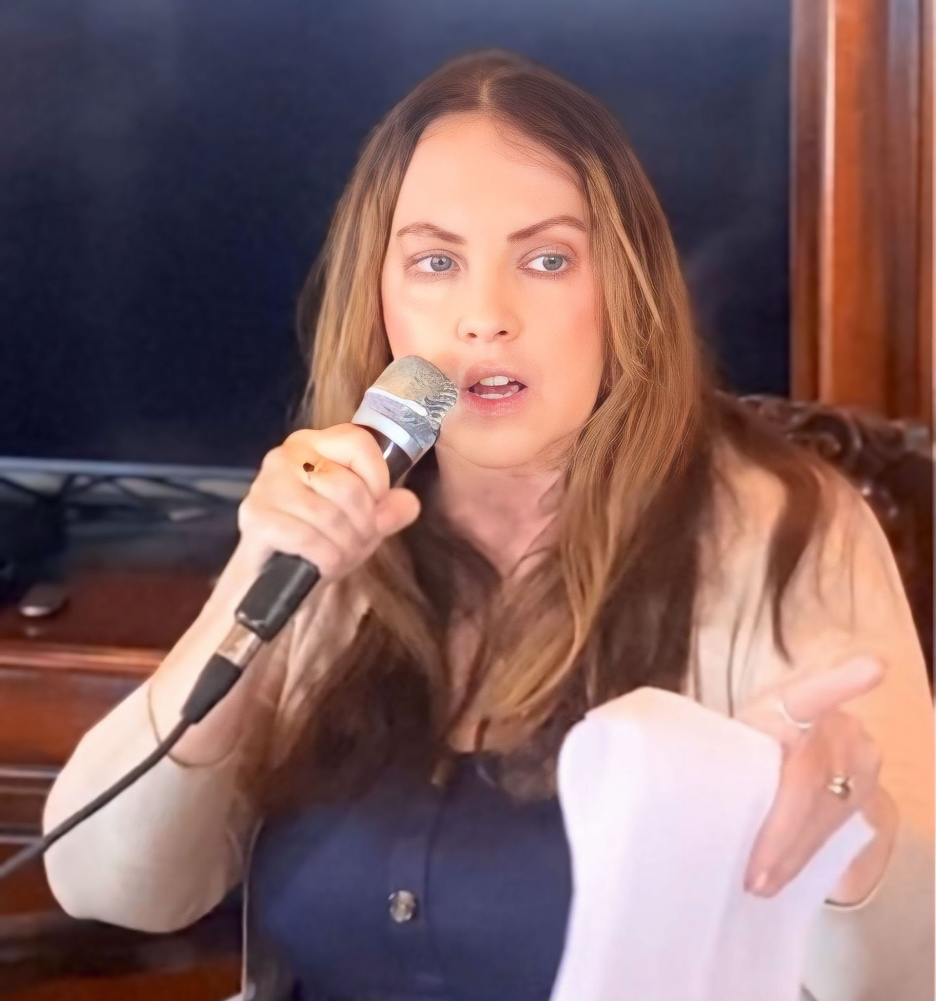 Woman holding a microphone and papers, speaking with a concerned expression.