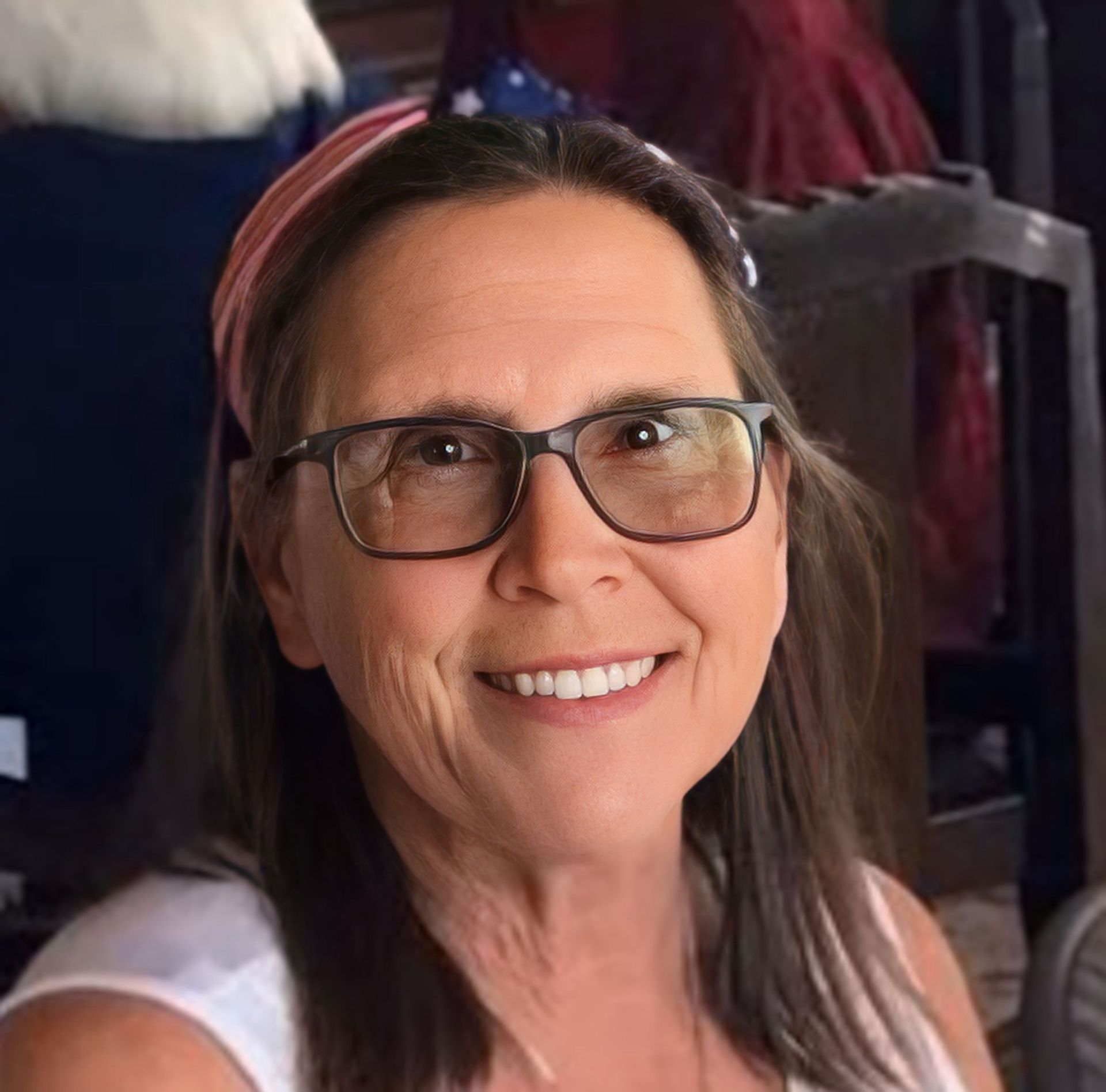 Woman with glasses and headband smiling, indoors.