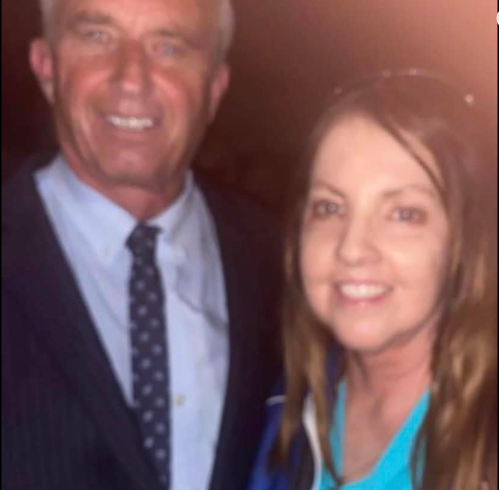 Robert F. Kennedy Jr. smiles next to a woman with long brown hair, both posing indoors.