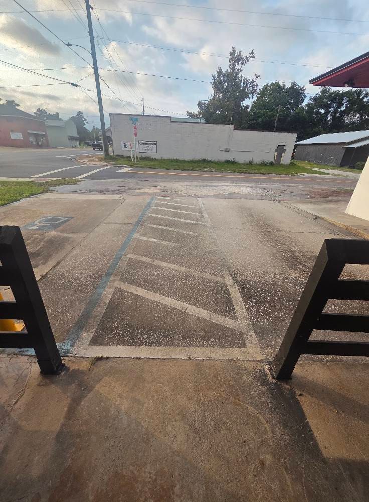 View from a building entrance toward a crosswalk and small businesses.  Grey pavement and cloudy sky.