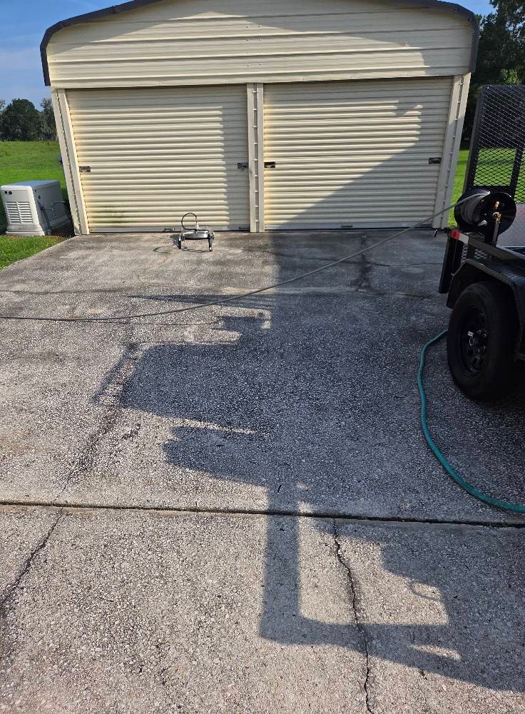 Garage with closed cream-colored doors on a gray concrete driveway with a trailer and pressure washer.