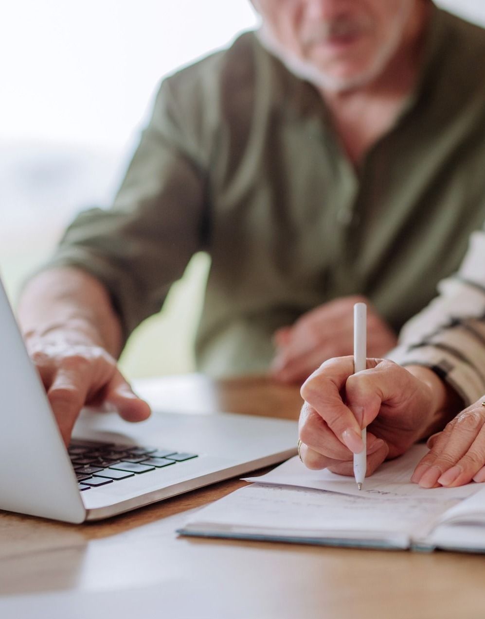 A man is using a laptop and a woman is writing on a piece of paper