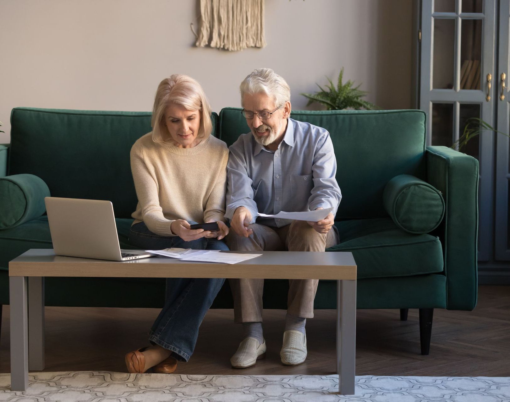 A man and a woman are sitting on a couch looking at a laptop.