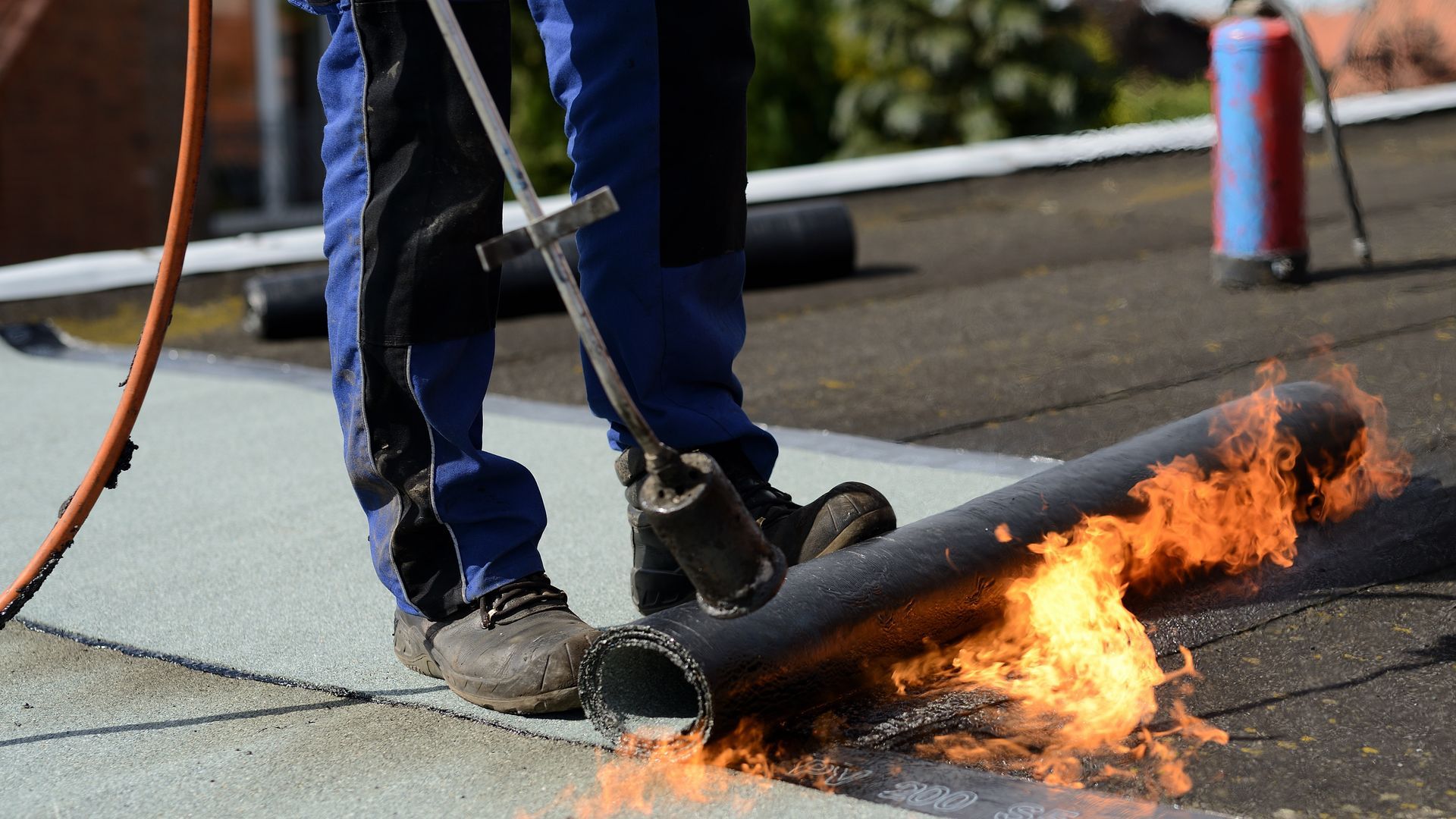 A man is using a torch to burn a roll of roofing.