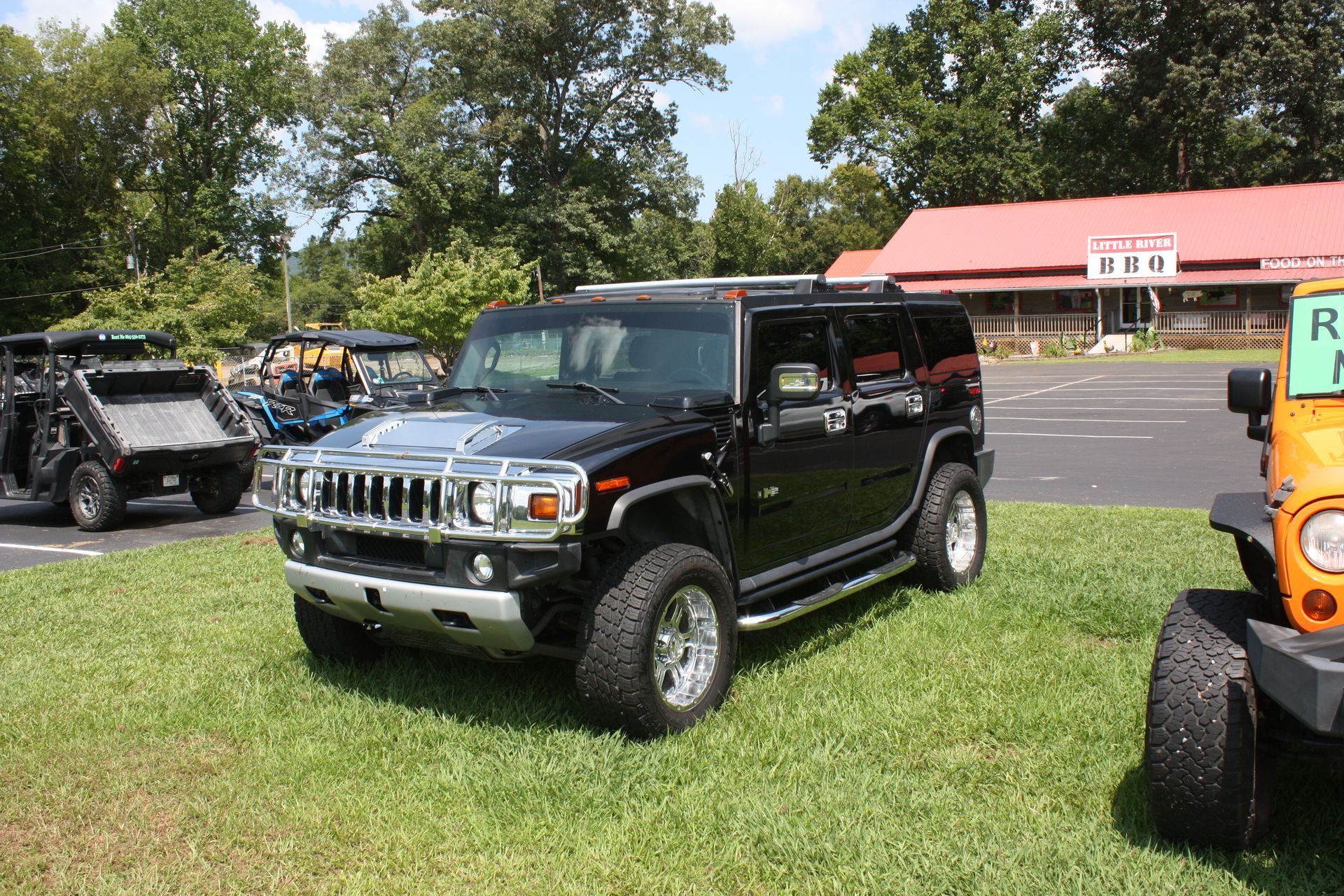 A black hummer is parked in the grass next to a yellow jeep.