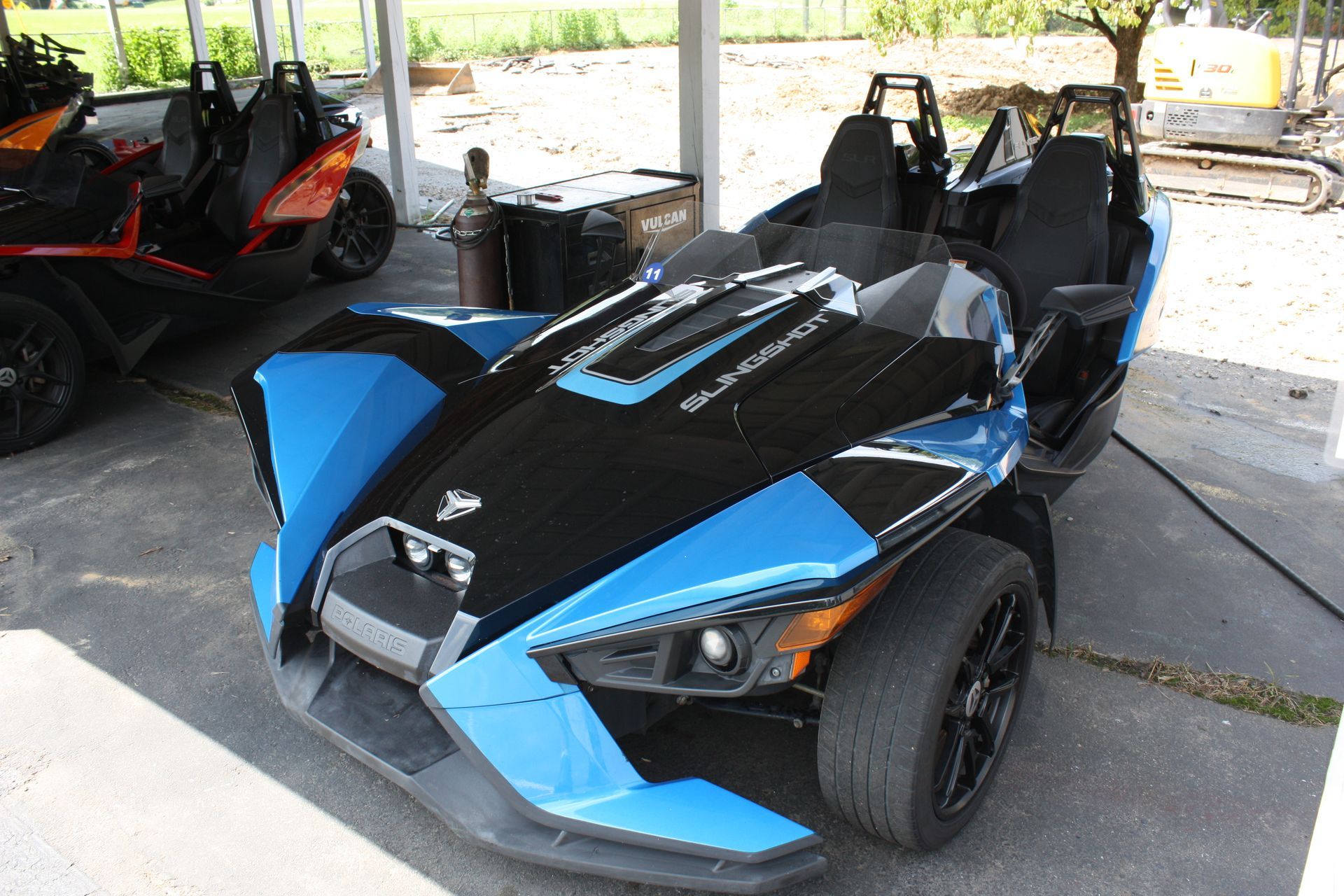 A blue and black slingshot is parked in a parking lot.