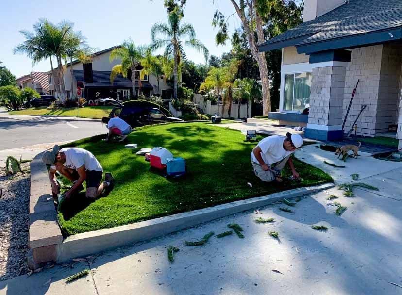 Three men are working on a lawn in front of a house.