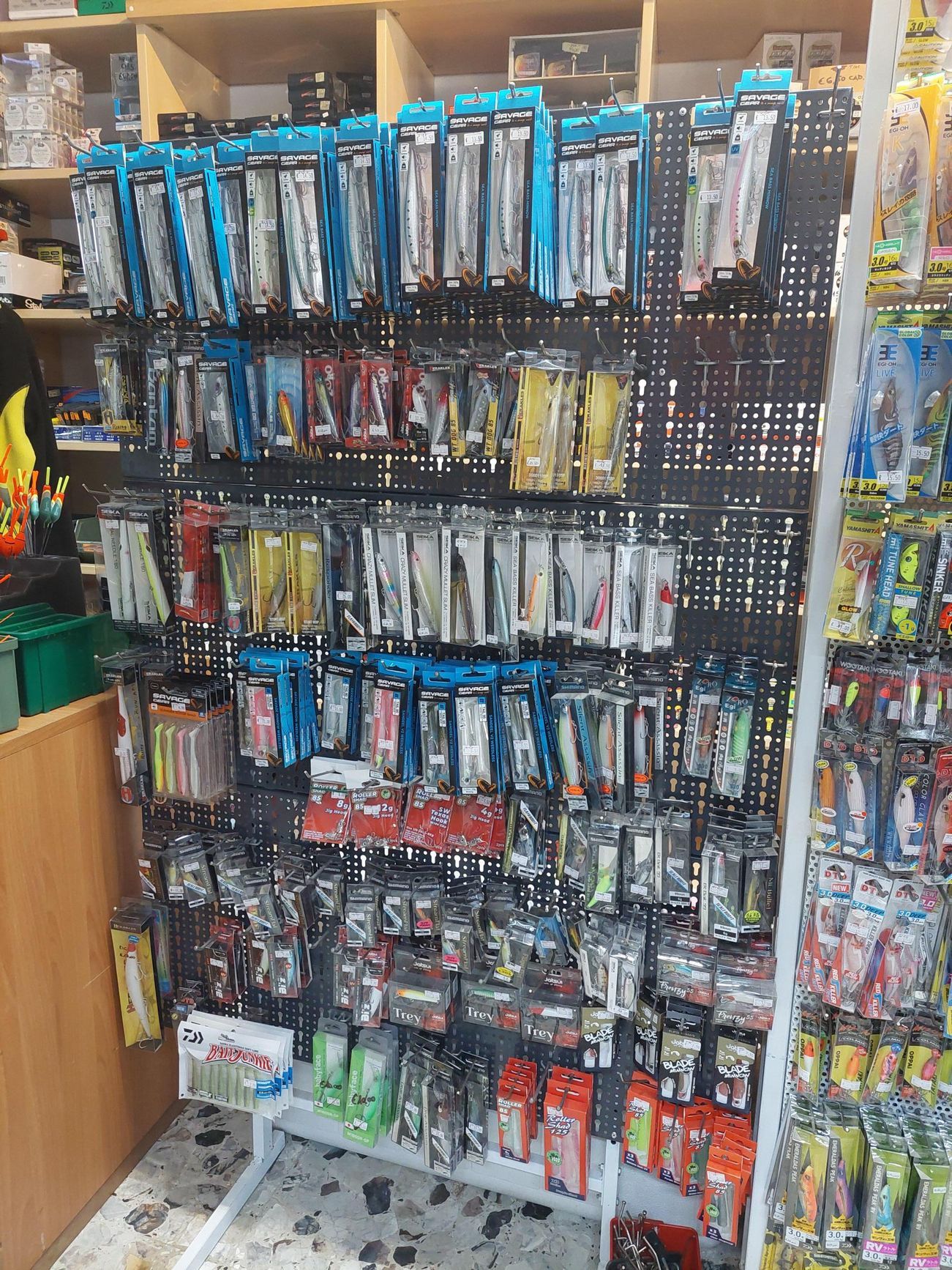 Esche da pesca esposte su un pannello forato nero all'interno di un negozio.