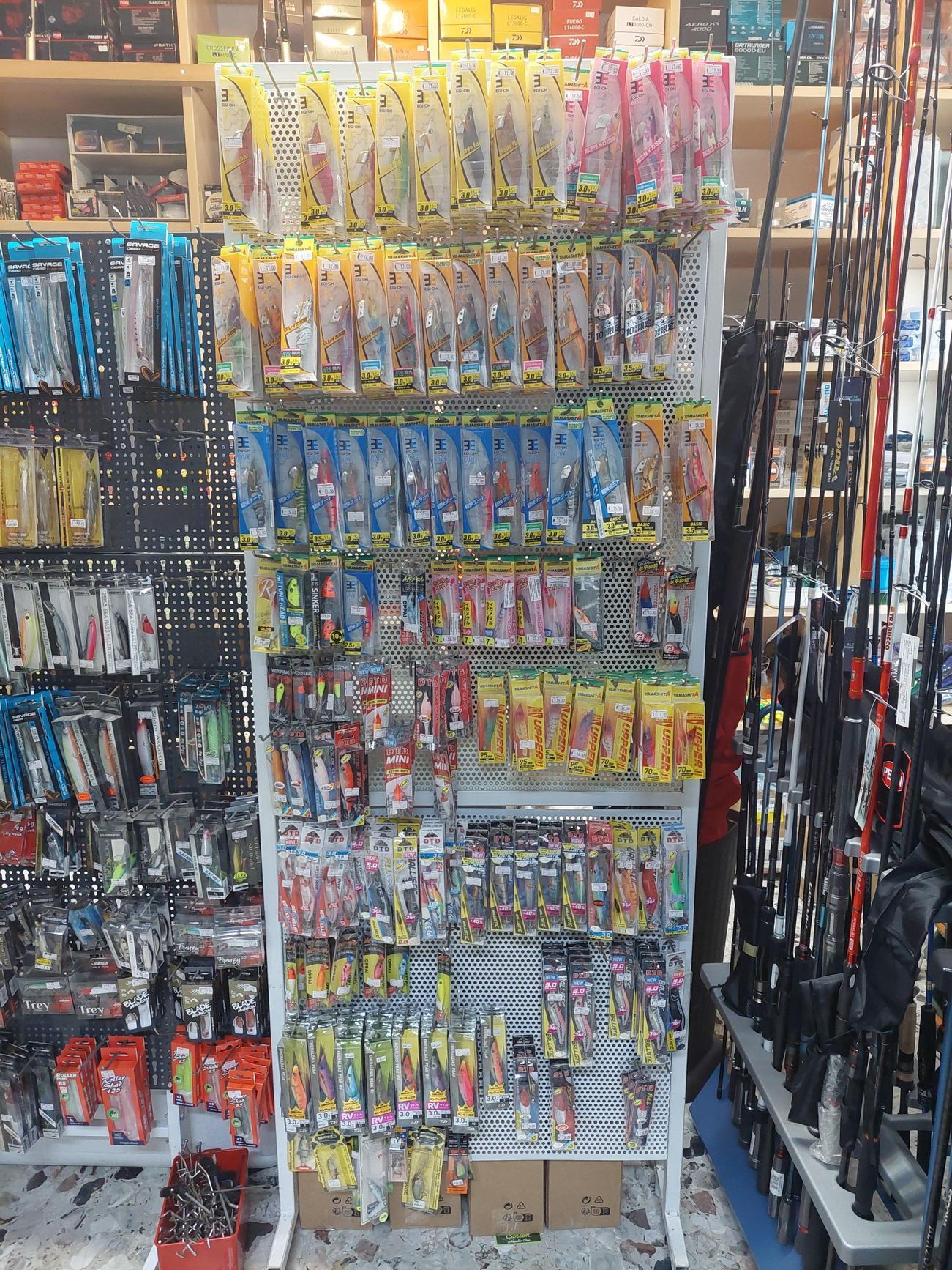 Esche da pesca esposte su uno scaffale di un negozio, di vari colori, insieme a canne da pesca.