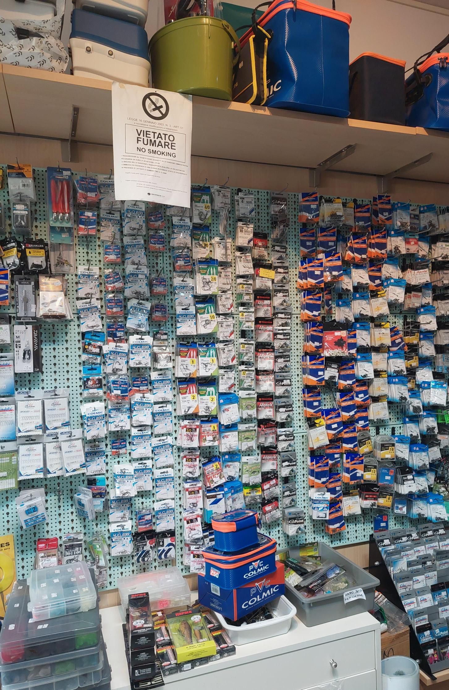 Parete espositiva di un negozio di attrezzatura da pesca. Numerosi piccoli articoli confezionati disposti su una griglia. Scatole per attrezzi blu e arancioni sugli scaffali.