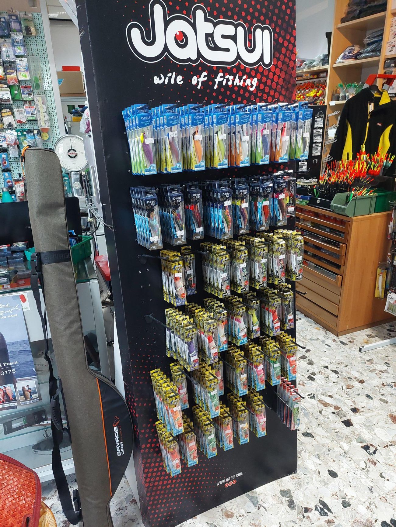 Esposizione di esche da pesca in un negozio; stand nero con file di esche colorate confezionate.