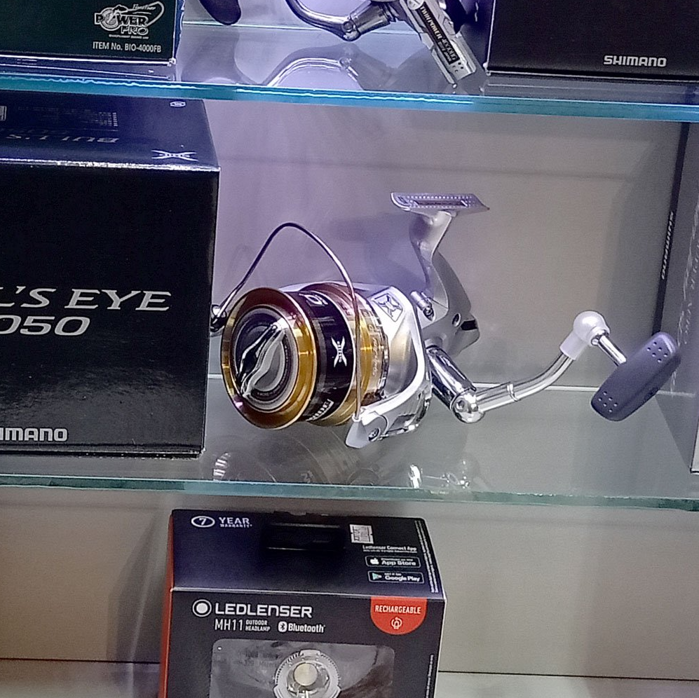 Mulinello da pesca su uno scaffale con scatole di prodotti.