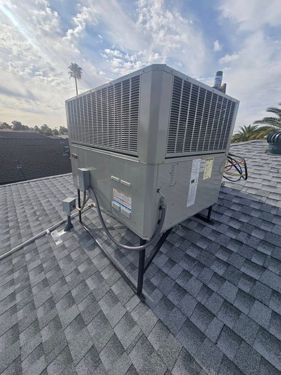 Rooftop air conditioning unit on gray shingled roof under a partly cloudy sky.