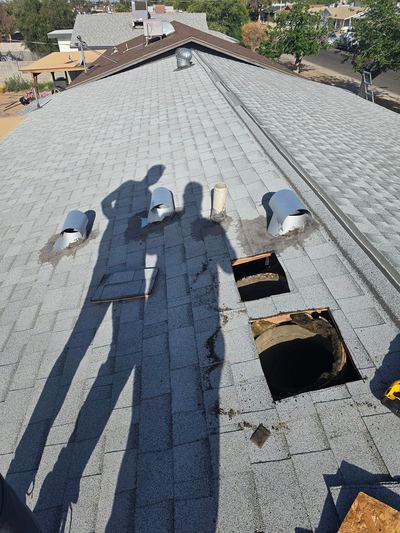 Shadows of people working on a gray shingled roof with open holes for ventilation.