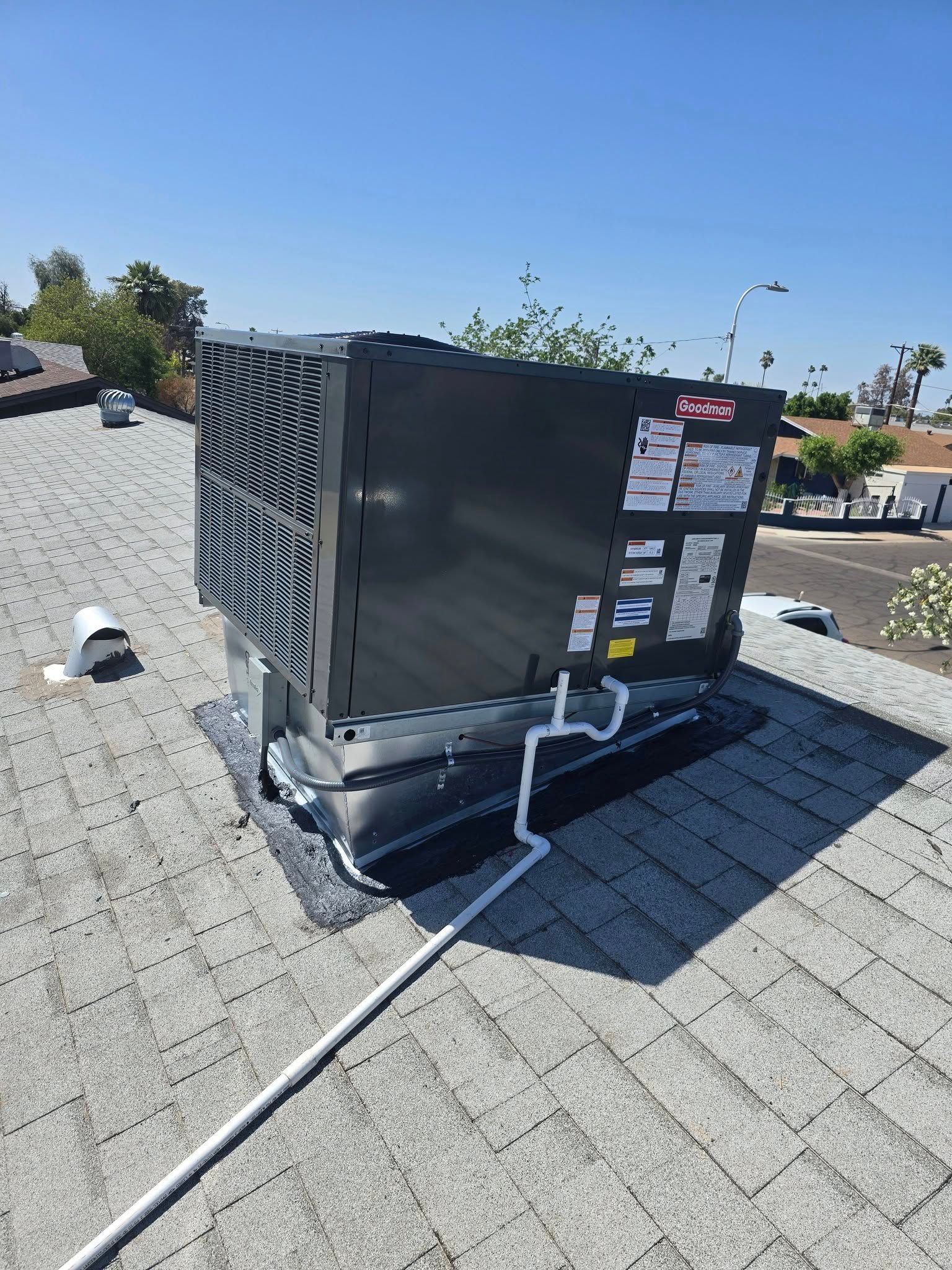 Rooftop HVAC unit on a shingled roof with white refrigerant lines and a clear blue sky.