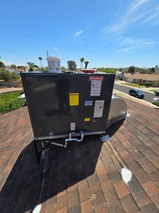 HVAC unit on a brown shingle roof, under a blue sky.