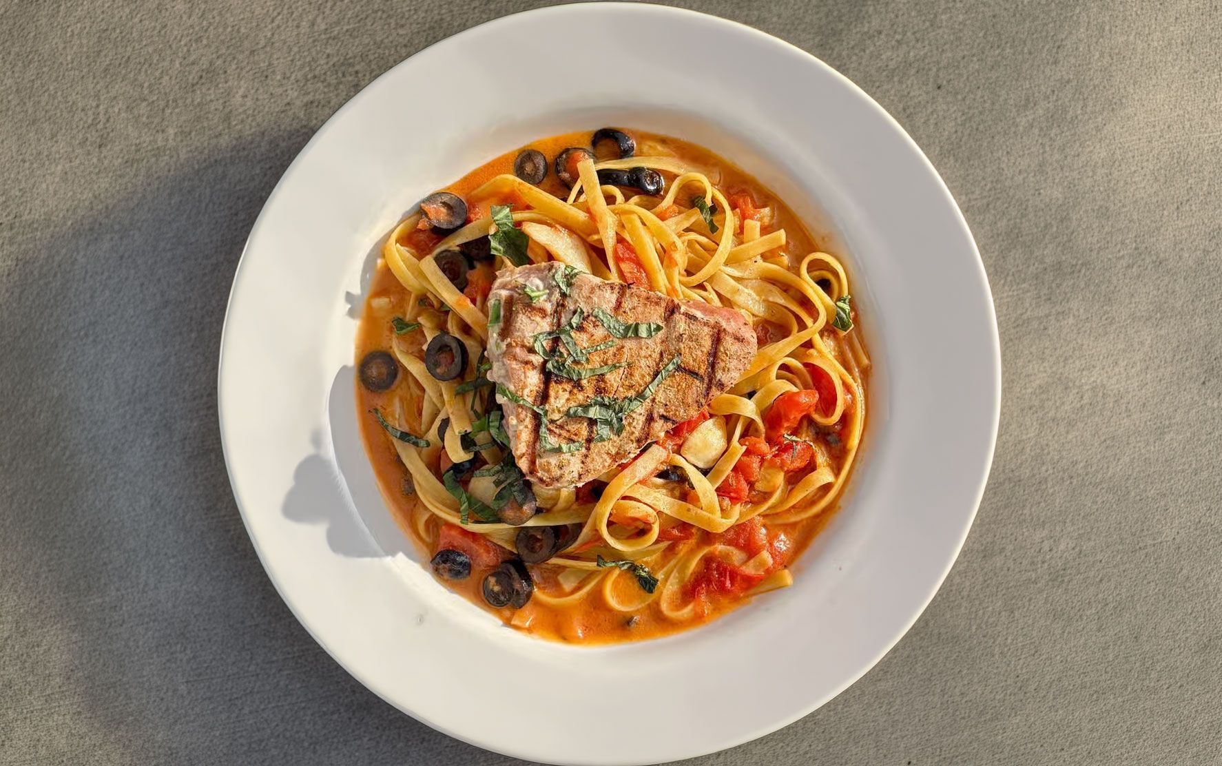Plate of spaghetti with tomato sauce, olives, and herbs on a white dish