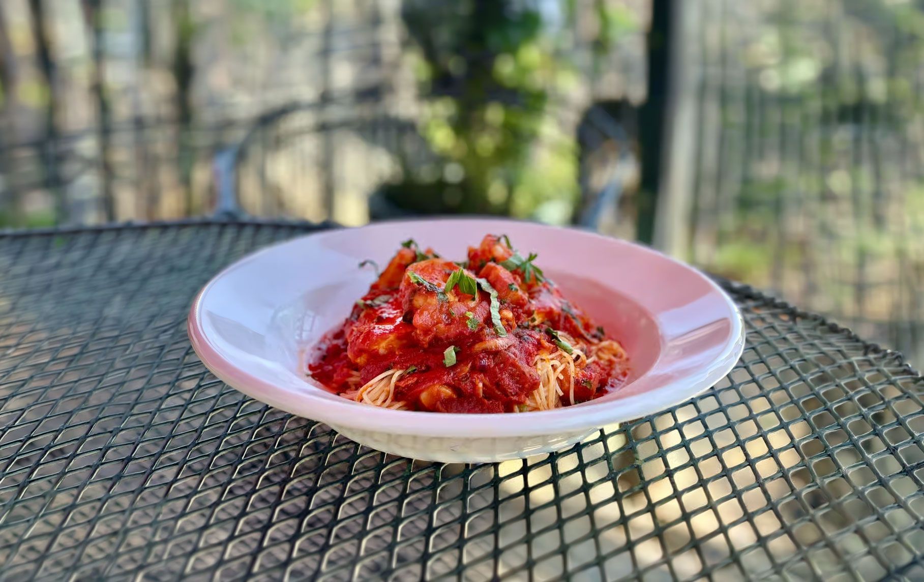 Red pasta dish topped with herbs on a white plate on an outdoor table