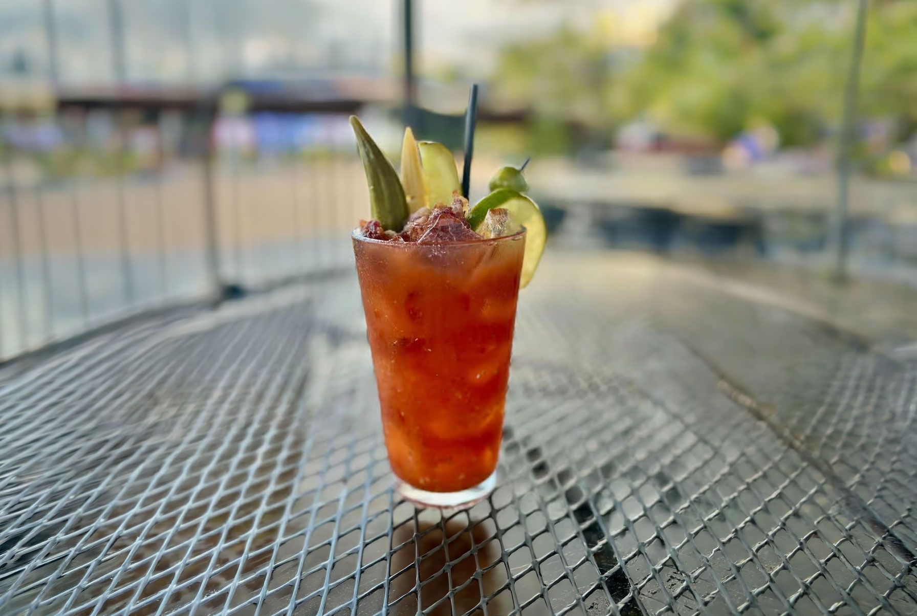 Tall iced red cocktail with mint and lime on a metal patio table, outdoors with blurred background