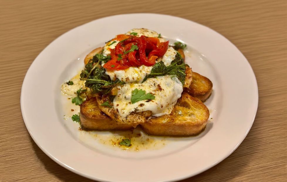Toasted bread topped with chicken parmesan, herbs, and red peppers on a white plate.