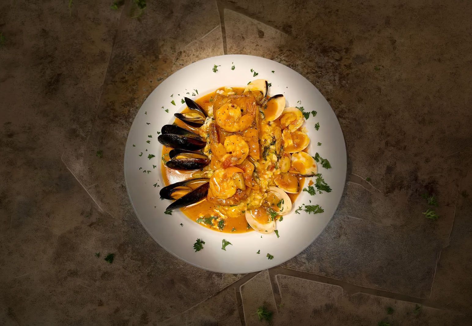 Overhead view of a white plate with orange seafood and black mussels, garnished with herbs.