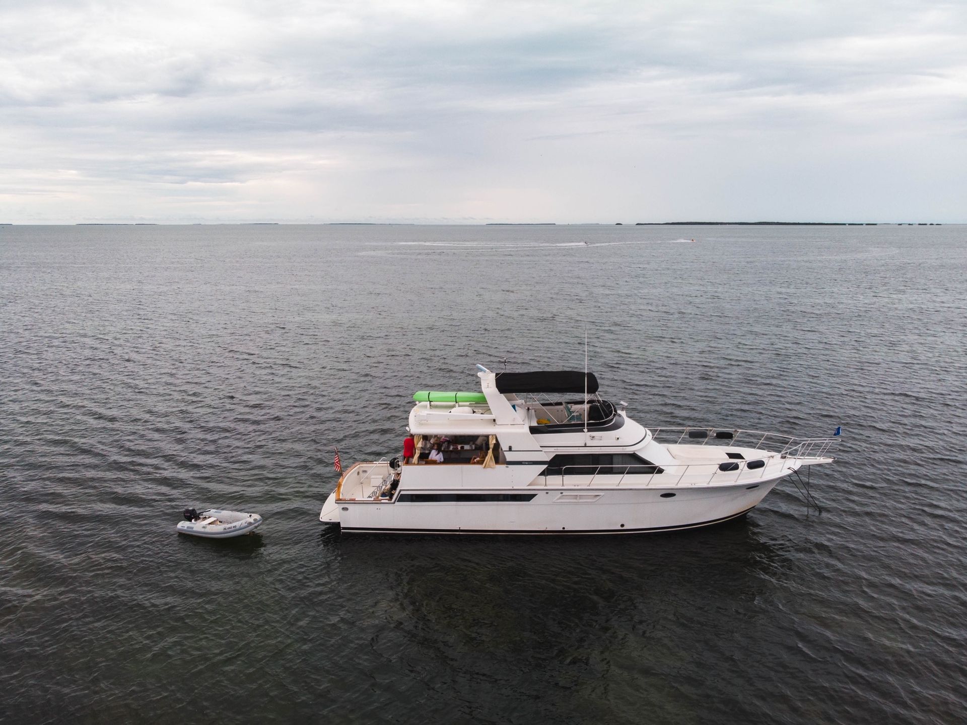 White yacht with a small dinghy on dark water under an overcast sky.