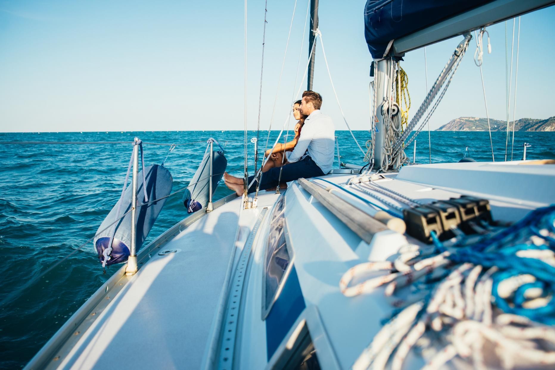Couple sitting on a sailboat, looking out at the ocean. Sunny day, blue water.