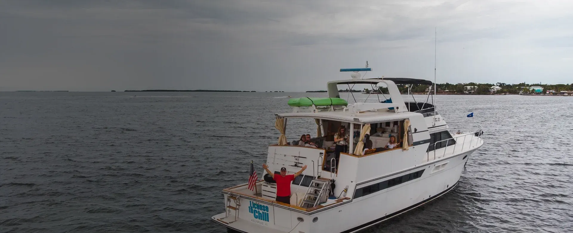 A white boat on the water with a person standing on the deck under a cloudy sky.