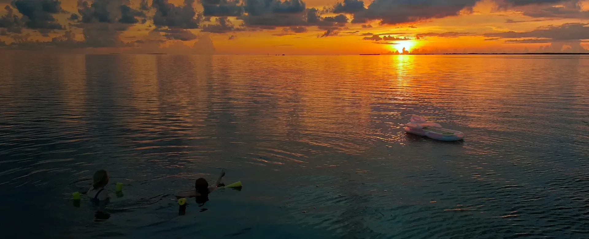 Sunset over water with two people snorkeling and a boat.