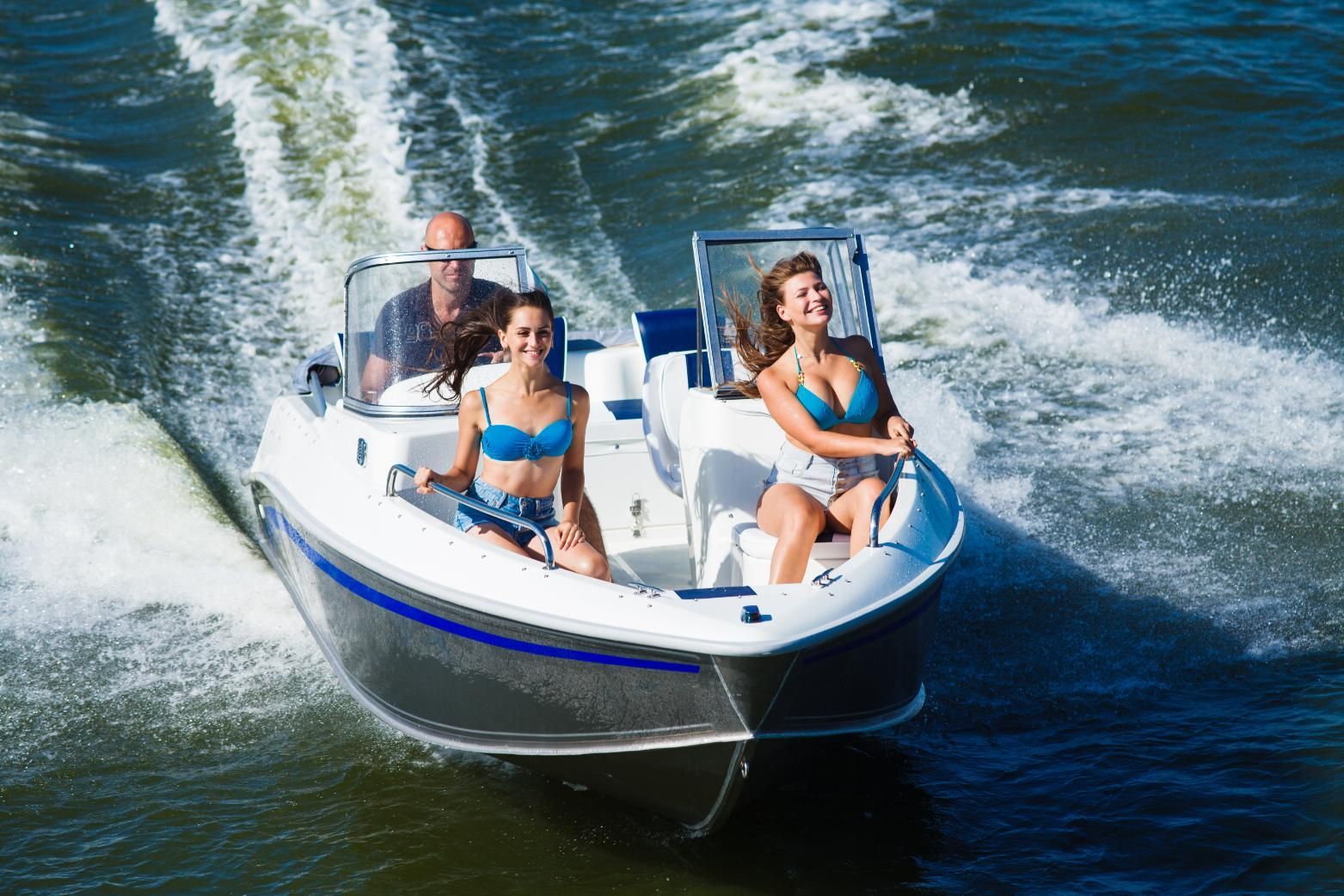A motorboat speeds across water with two women and a man enjoying the ride.