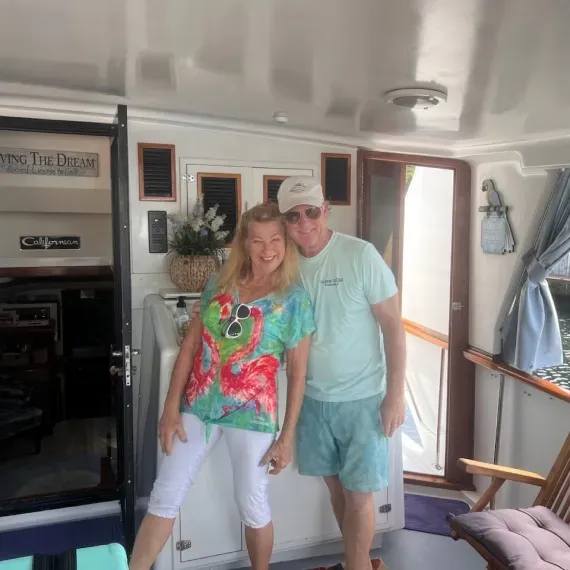 Couple on a boat deck, woman in colorful top, man in blue shorts, smiling.