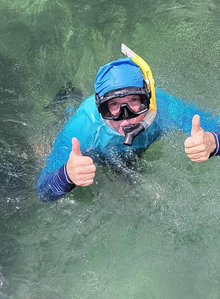 Person snorkeling in clear water gives thumbs up.