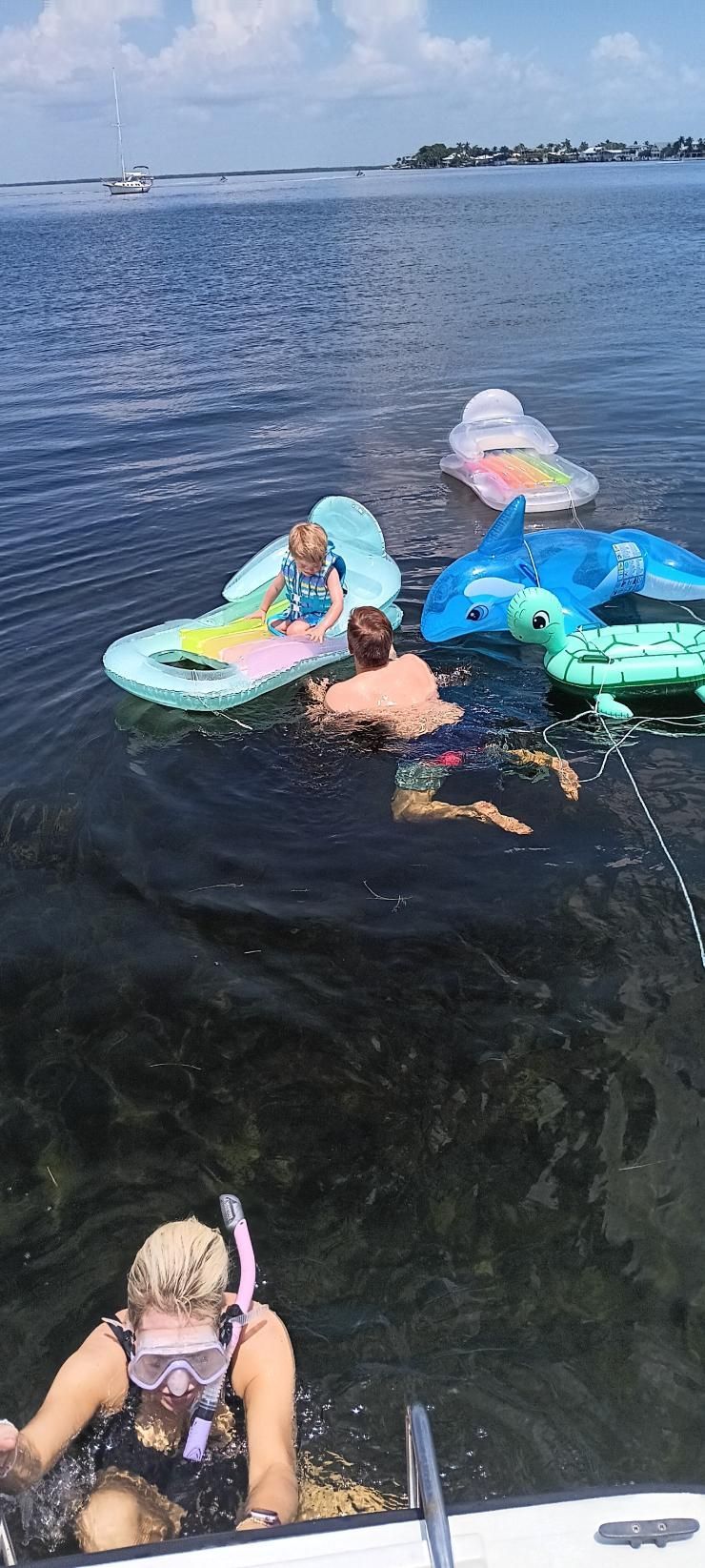 People swimming near a boat and floats on a body of water under a blue sky.
