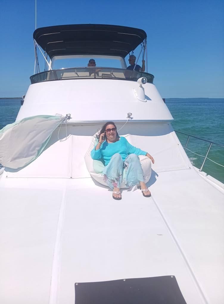 Woman sitting on a white yacht deck, talking on the phone; blue sky and water.