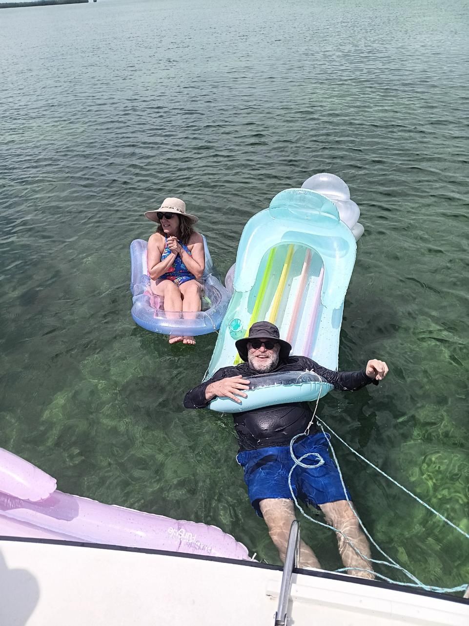 People floating in clear water on inflatable rafts. A person in a hat pulls on a rope.