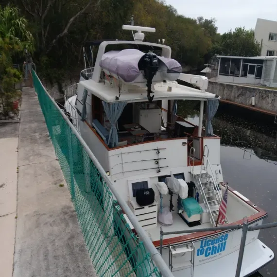 White boat docked in a canal, green fence, trees, and buildings in the background. 