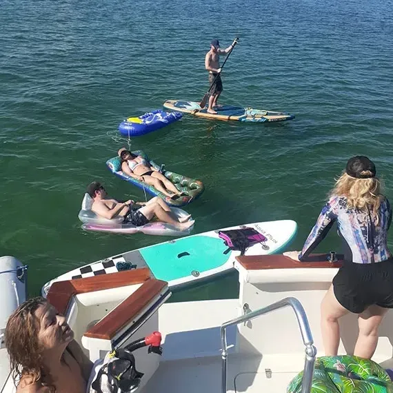 People enjoying a sunny day on water, using paddleboards, and floating on rafts near a boat.