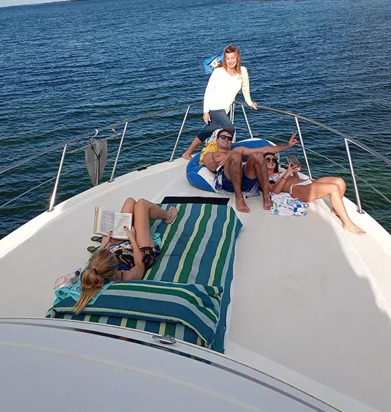 People on a boat enjoy sun, ocean view. Some sunbathe, read, and relax.