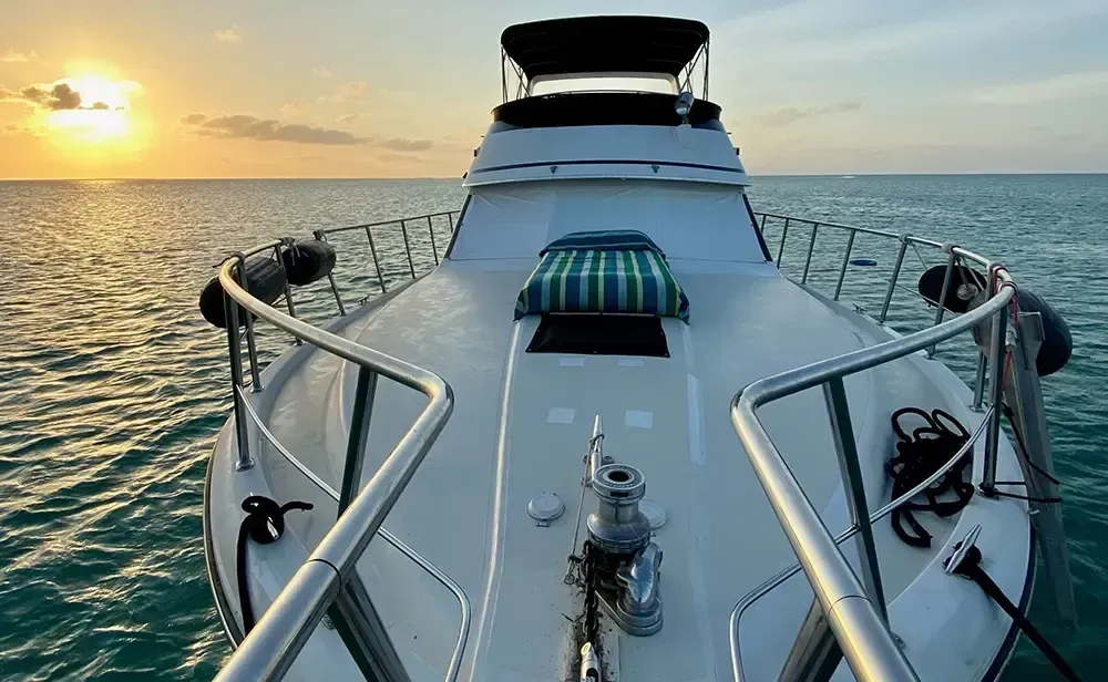 White yacht on calm water with a sunset in the background.