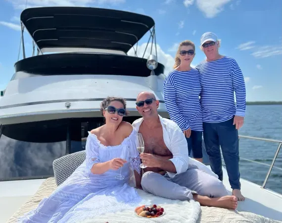 People on a yacht; two seated, one holding champagne; two standing in striped shirts.