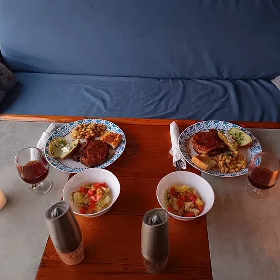 Two plates of food, salad, and wine glasses on a table in front of a blue couch.