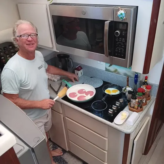 Man cooking eggs and pancakes in small kitchen.