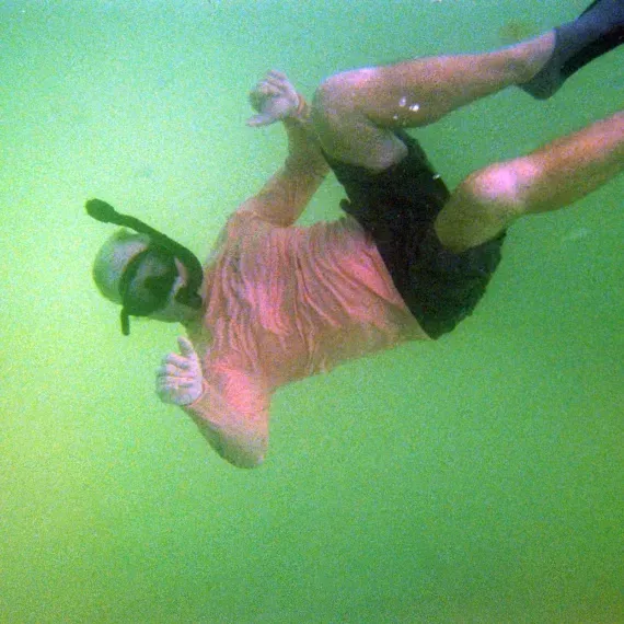 Person underwater snorkeling, wearing snorkel mask, giving the 