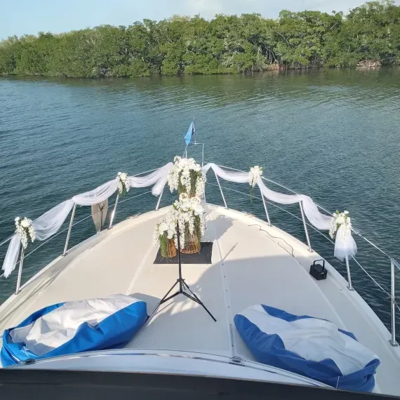Boat bow decorated for a wedding ceremony with floral arrangements, white fabric, and mangrove trees in the background.