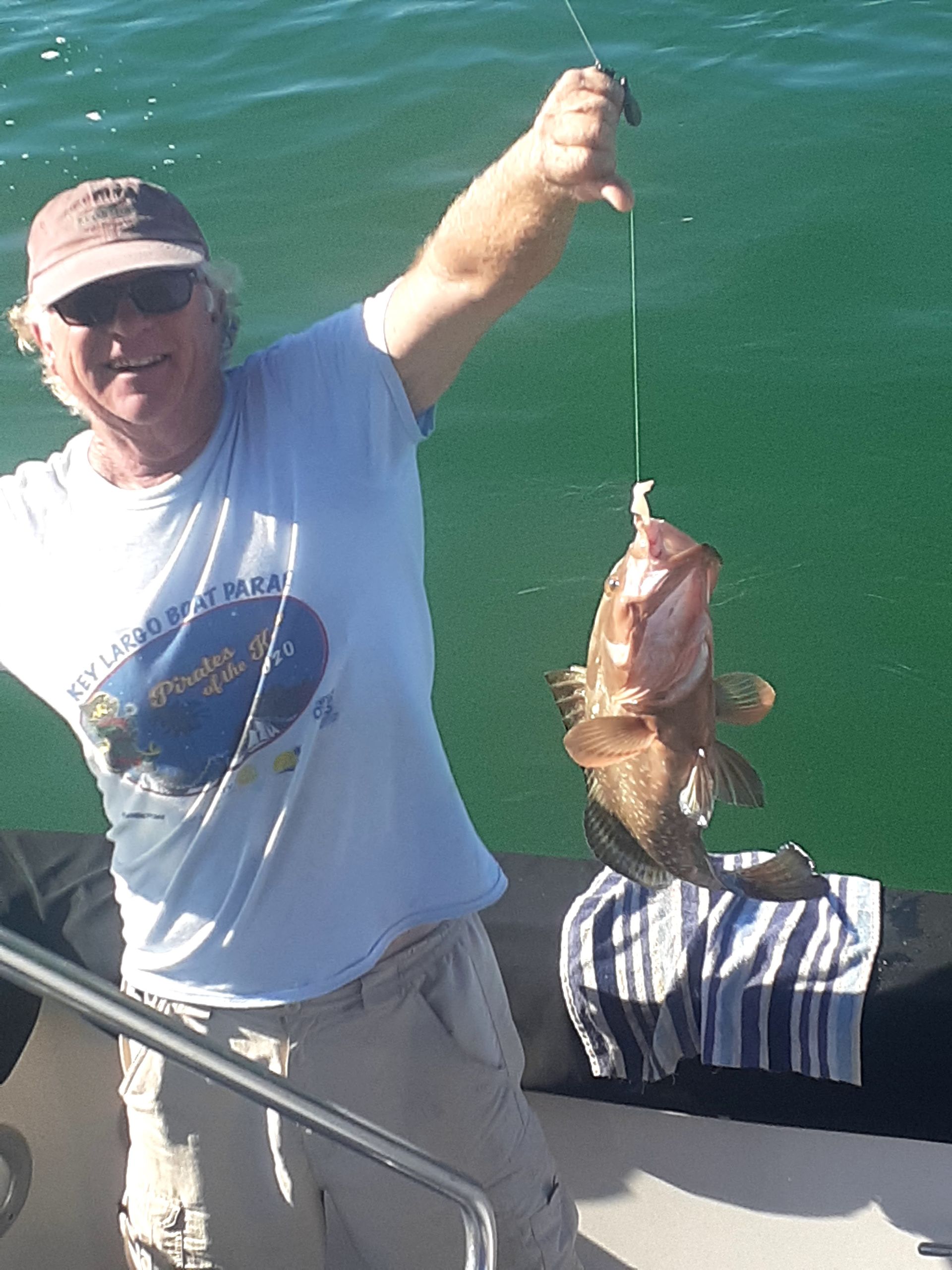 Man on a boat holds up a brown fish by fishing line, smiling.