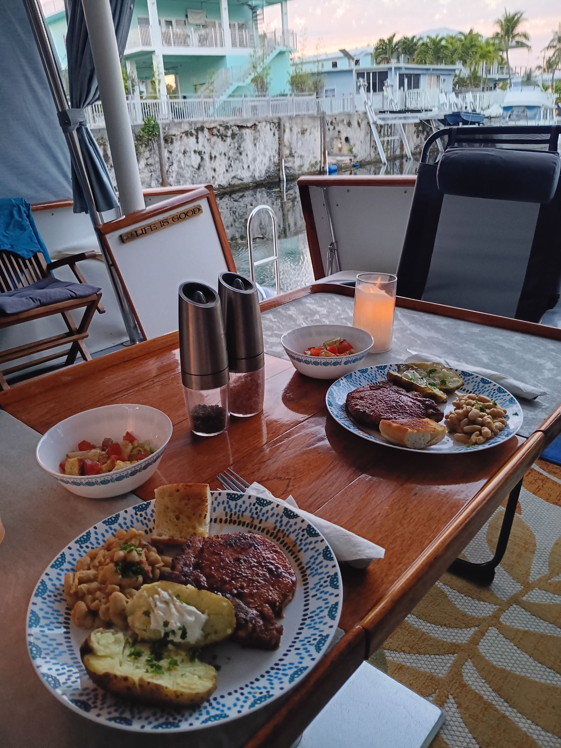 Dinner on a boat at dusk: steak, sides, two plates, salt & pepper shakers, water views.