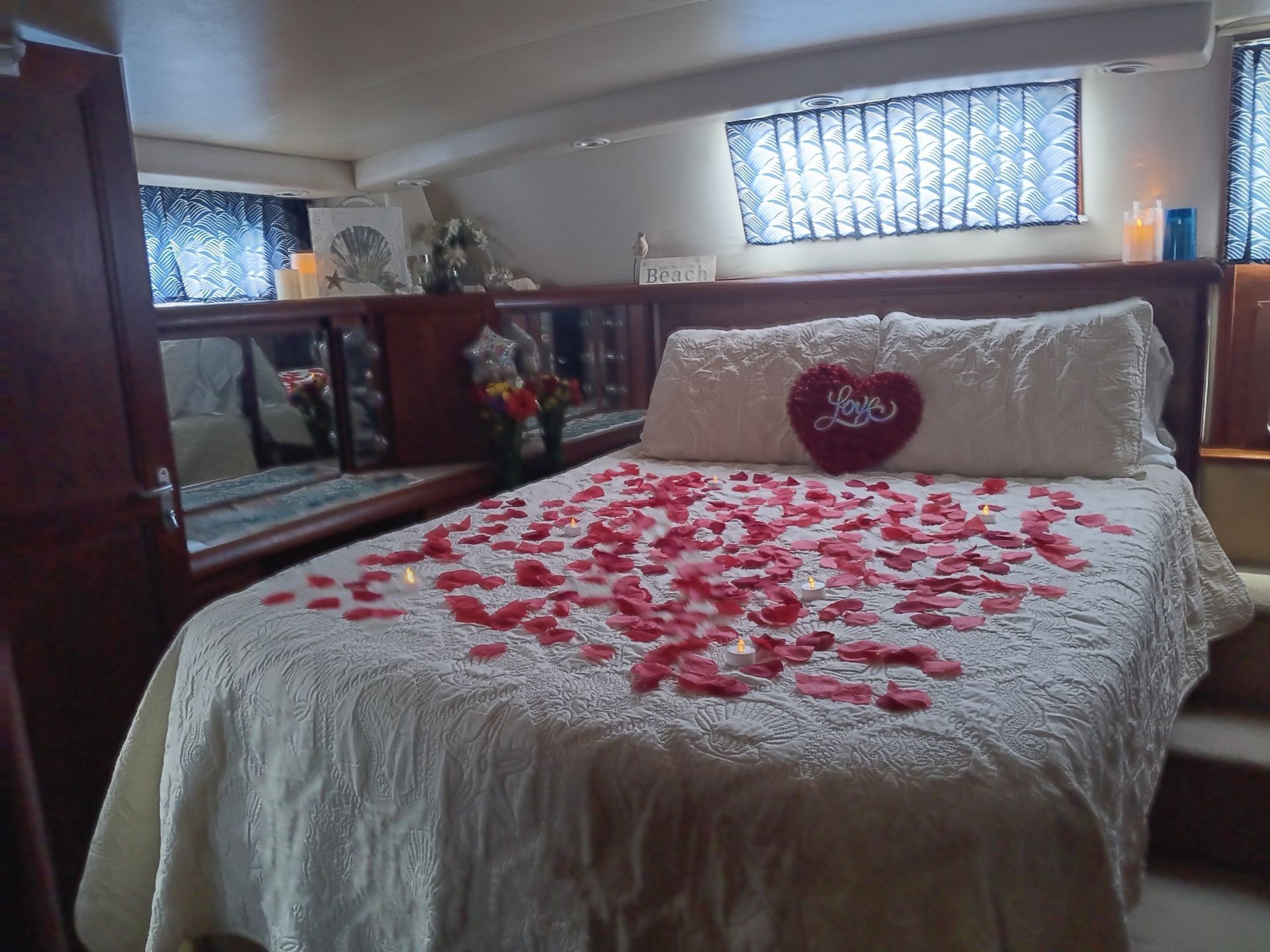 A bed decorated with rose petals and a heart-shaped pillow, inside a boat cabin.