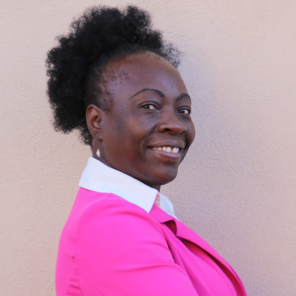 A Black man in a navy suit and tie, smiling, indoors with a red backdrop.
